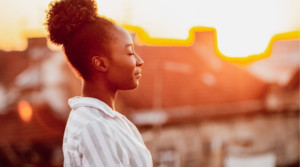 An adult woman with her eyes closed standing in front of a sunset